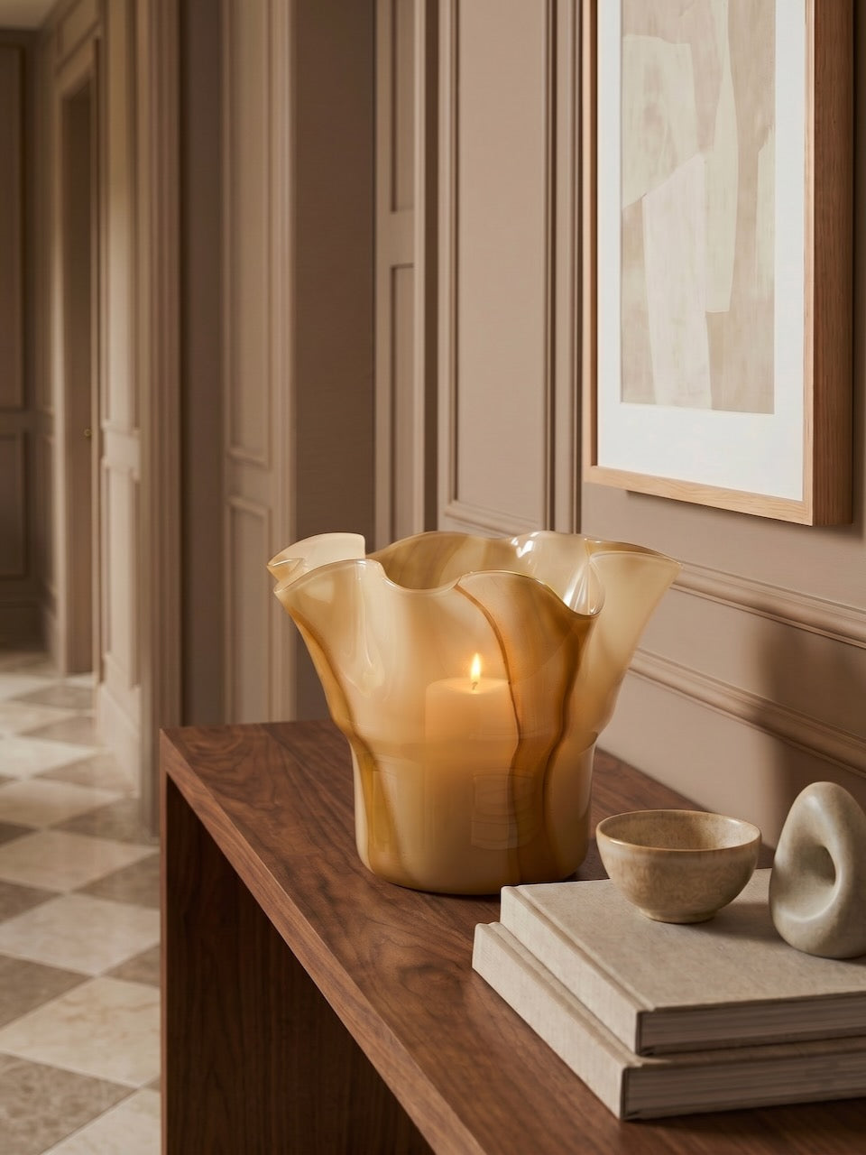 Decorative vase with a candle on a wooden surface in a room with framed artwork.