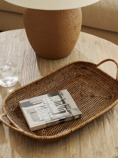 Antique brown rattan tray with handles, handwoven rectangular serving tray styled on coffee table with books and decor