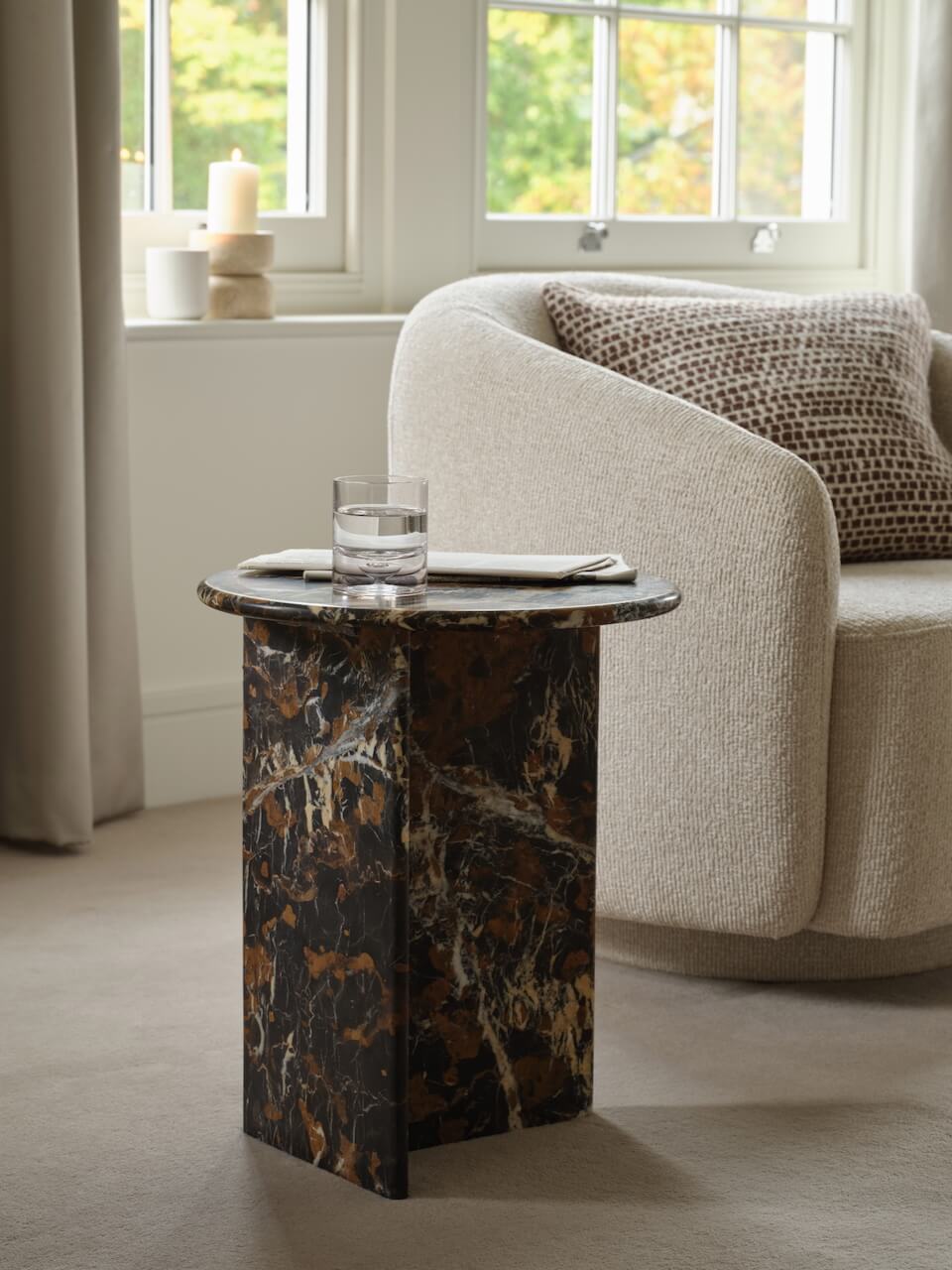 A brown marble side table with a cylindrical shape, placed in a living room setting with a glass of water on top.