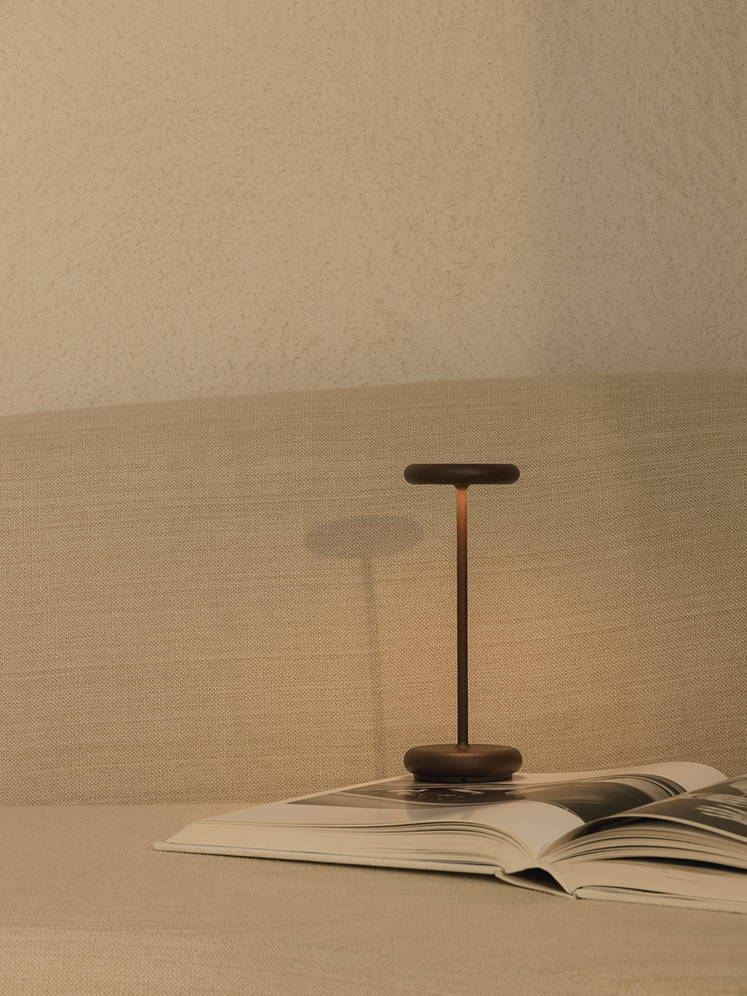 Lana rechargeable table lamp in corten finish styled on sofa with book creating soft ambient lighting cordless dimmable lamp for modern living room