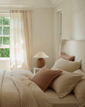 Neatly arranged bedroom with a bed, armchair, and window with white curtains.