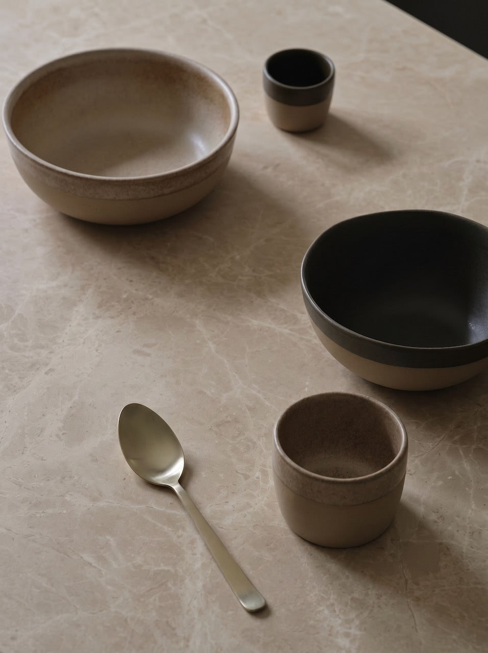 Set of ceramic bowls and a spoon on a textured surface