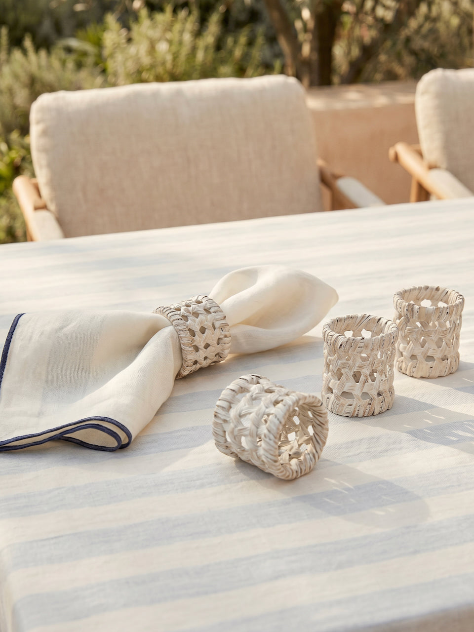 Close-up of handwoven white rattan napkin rings paired with a cream linen napkin on a striped tablecloth, showcasing the intricate artisan weave and natural texture.