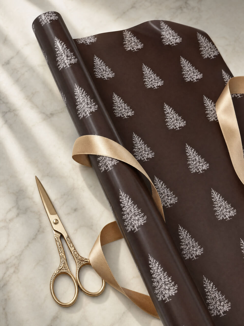 A roll of dark brown wrapping paper with a repeating white pine tree pattern, partially unrolled on a light marble surface with gold scissors and a beige ribbon.