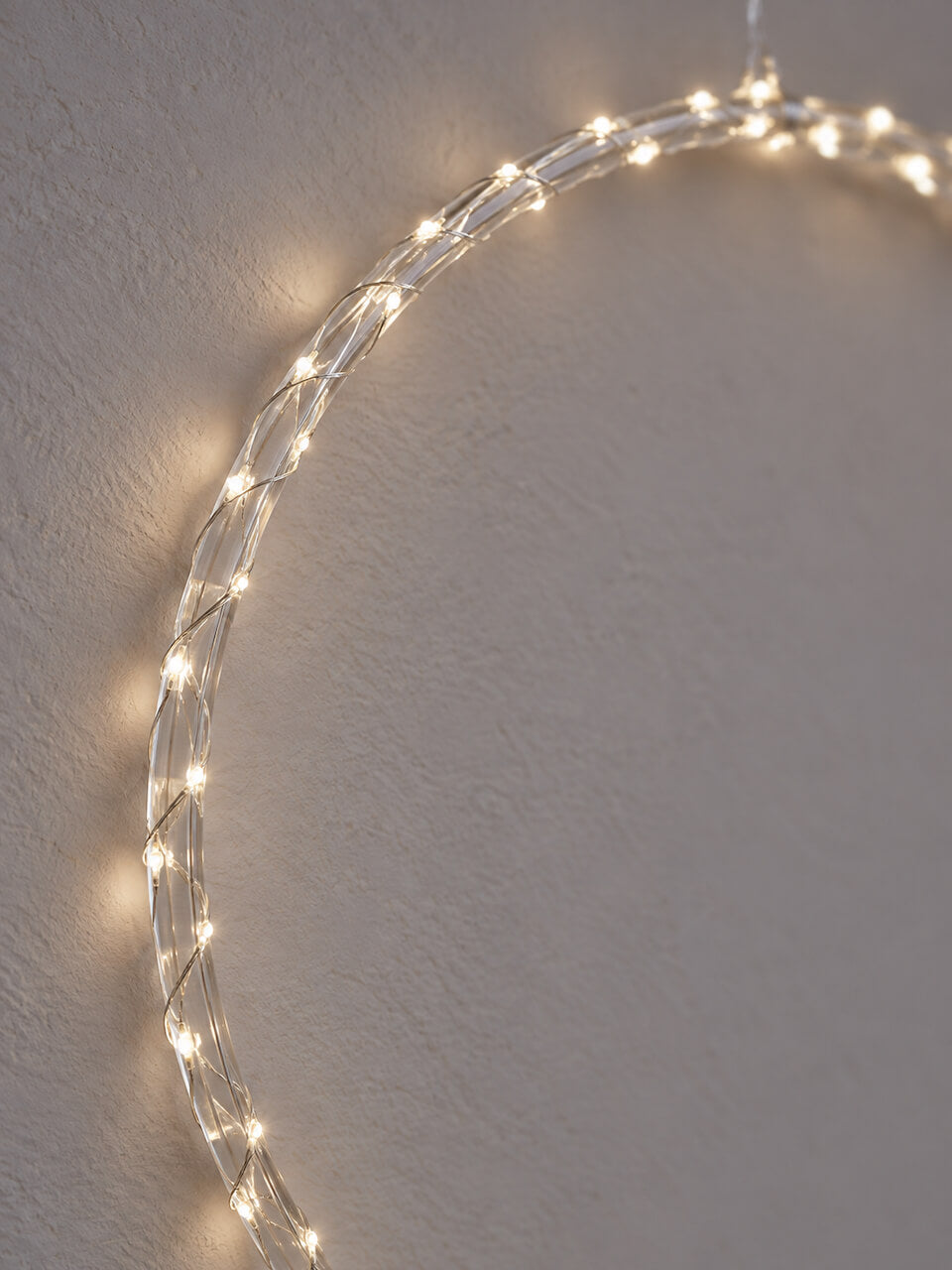 Twisted wire string lights with warm white LED bulbs, draped in a large semi-circle against a textured light gray wall.