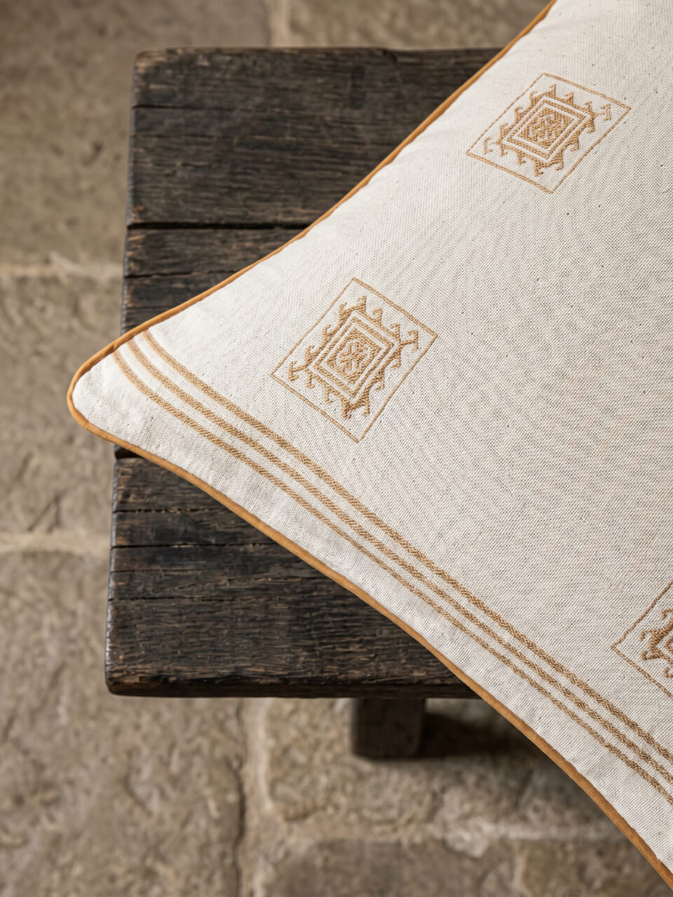 Close-up detail of a luxury cream and caramel patterned cotton cushion cover with woven geometric detailing and caramel piping, styled on rustic timber for a warm contemporary aesthetic.