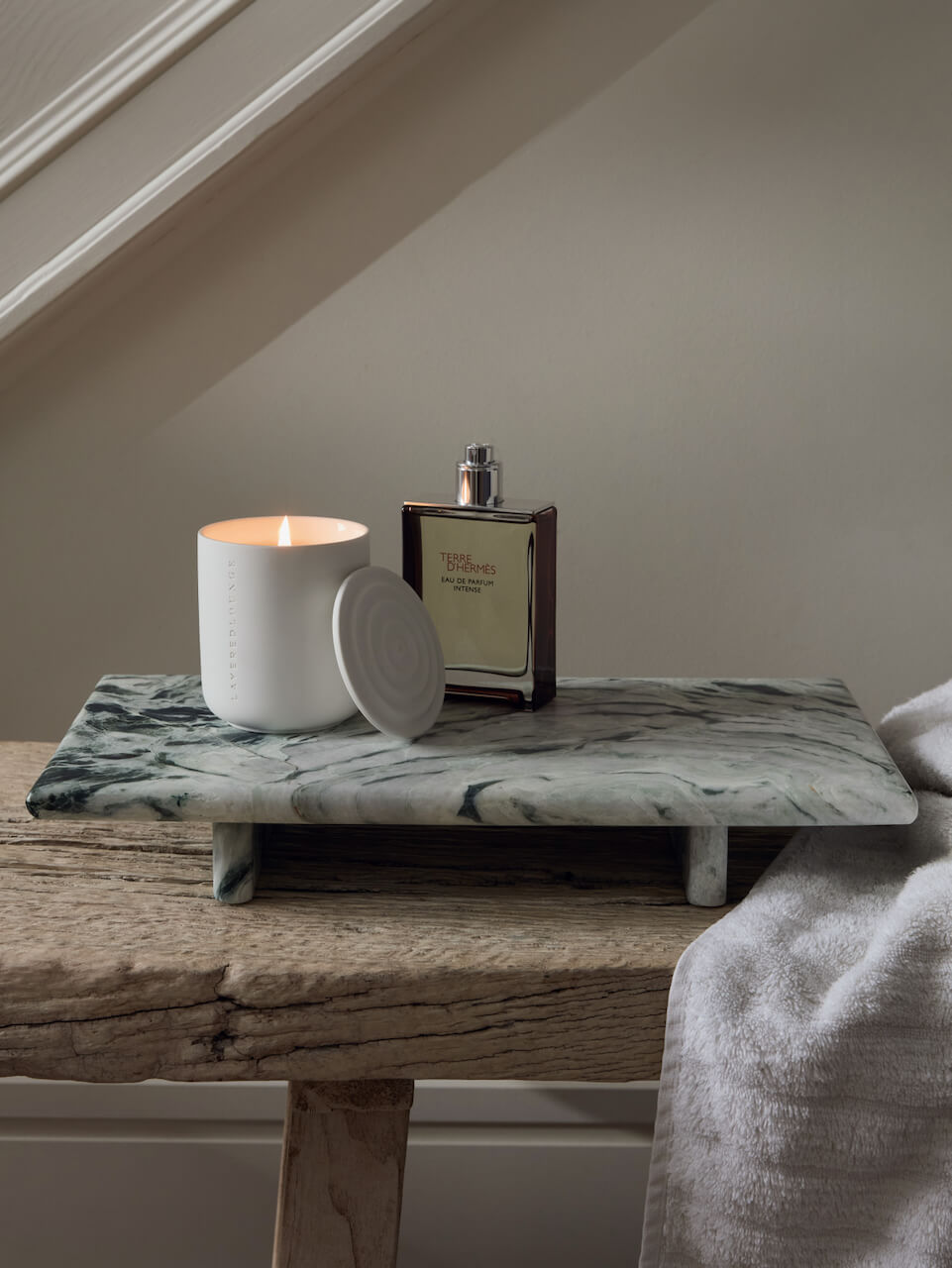 Candle and perfume bottle on a marble tray with wooden surface and neutral wall background