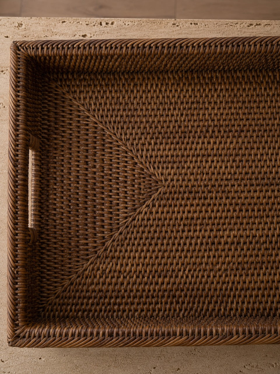 Antique brown rattan tray detail close-up showing the intricate handwoven weave pattern and integrated handle, styled on a travertine surface in warm natural light.