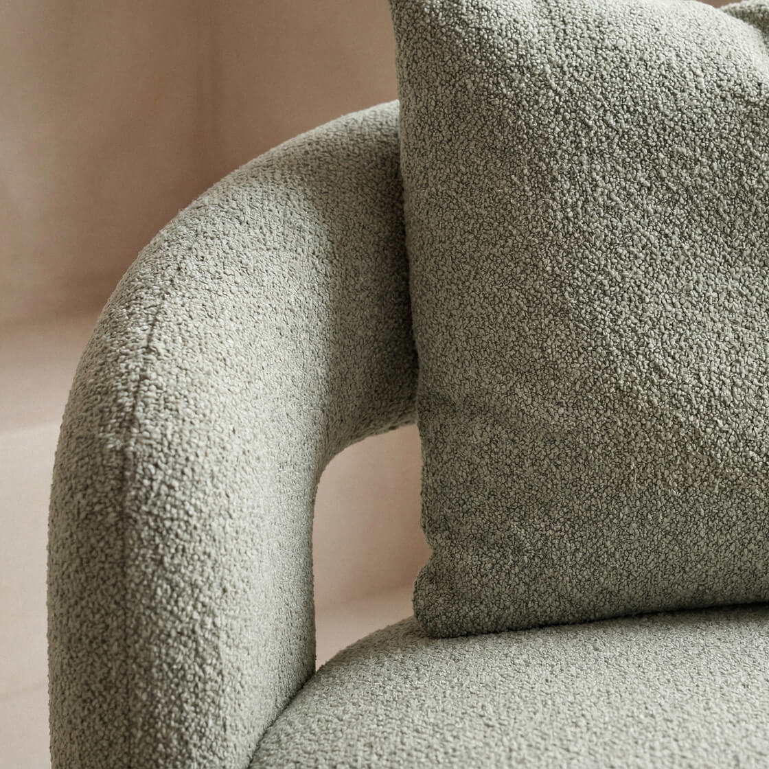 Close-up of a textured boucle upholstered armchair in a muted sage green color, featuring a matching textured throw pillow.