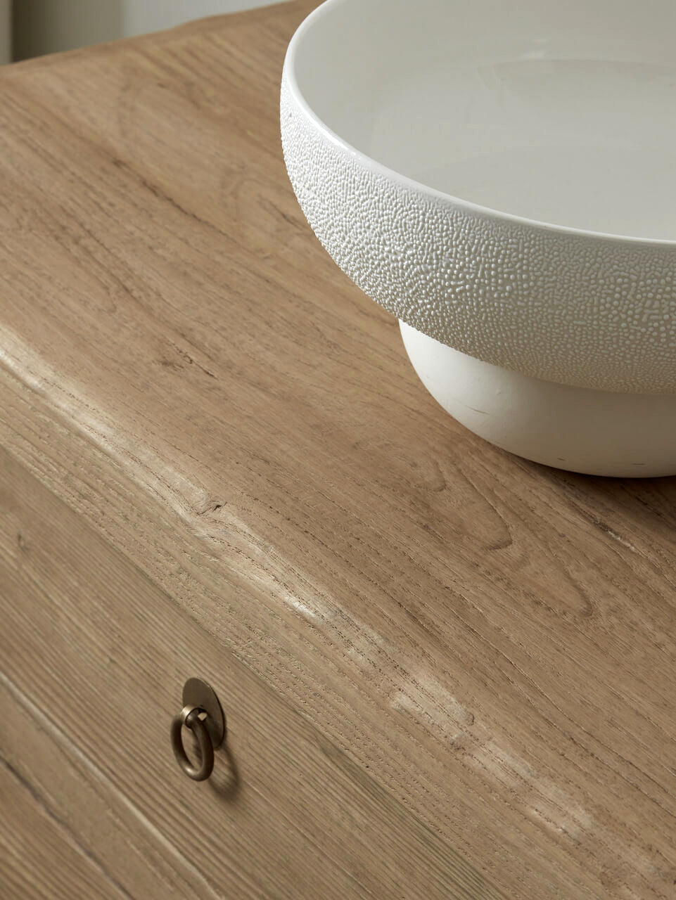 White textured bowl on a wooden surface with a metal handle.