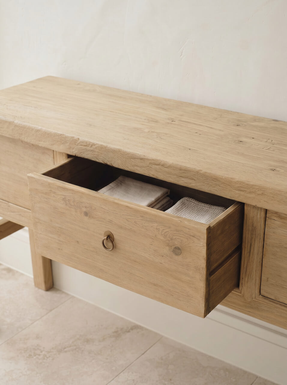 Wooden bench with a drawer open, revealing folded clothes inside, on a light-colored floor.
